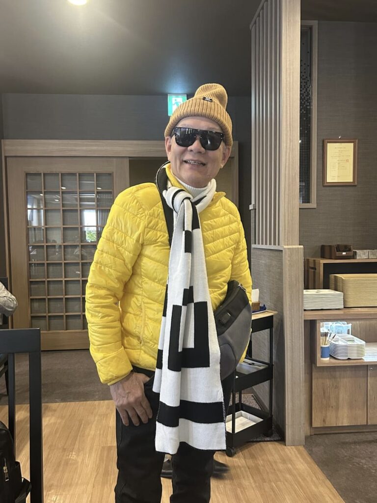 A tour guest in a yellow jacket and striped scarf smiling inside a Japanese restaurant.