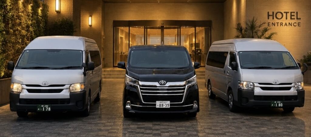 Three luxury tour vehicles parked at night under warm lighting outside a hotel entrance: a black Toyota Alphard in the center flanked by two silver Toyota HiAce vans.